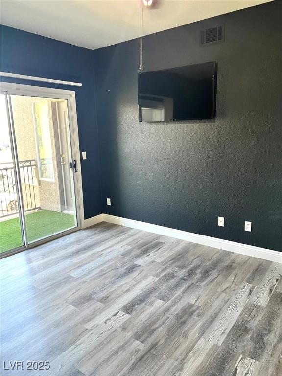 unfurnished room with visible vents, a textured wall, baseboards, and wood finished floors