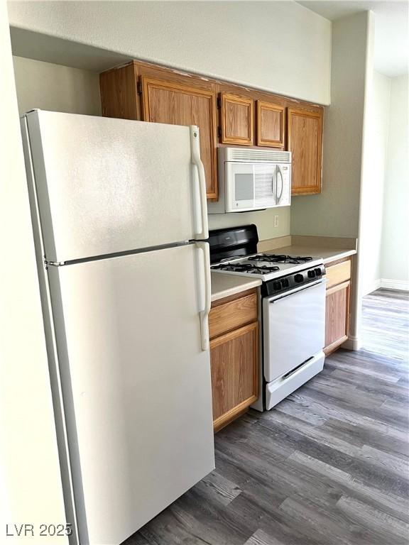 kitchen featuring light countertops, white appliances, dark wood-type flooring, and brown cabinets