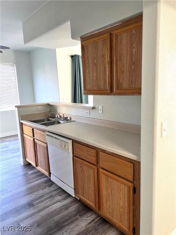 kitchen featuring brown cabinetry, dark wood finished floors, white dishwasher, light countertops, and a sink