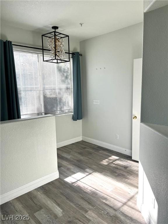 unfurnished dining area with a notable chandelier, baseboards, and wood finished floors