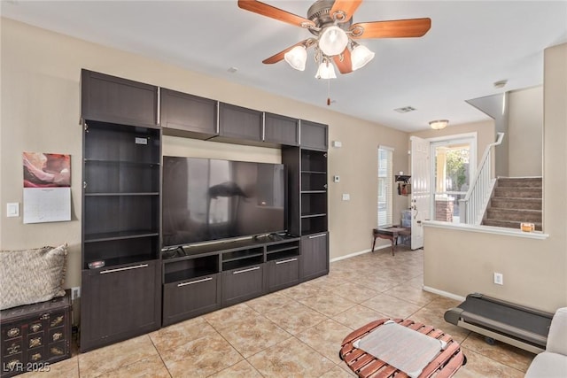 living room with light tile patterned floors, baseboards, visible vents, ceiling fan, and stairs