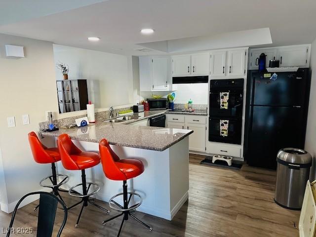 kitchen featuring light stone counters, a peninsula, black appliances, a kitchen bar, and white cabinetry