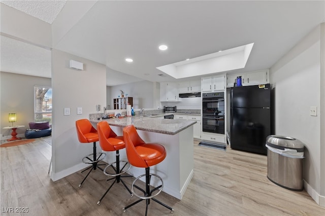 kitchen featuring light wood-type flooring, black appliances, a sink, a peninsula, and a skylight