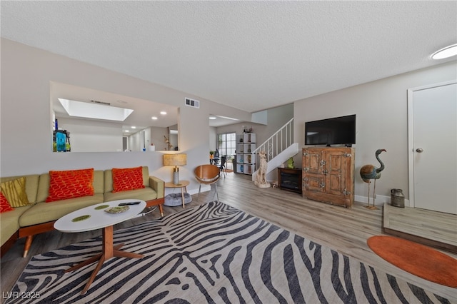 living room featuring wood finished floors, visible vents, a skylight, stairs, and a textured ceiling