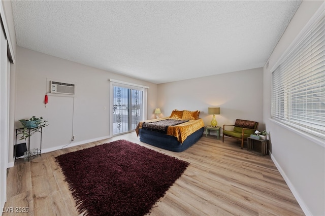 bedroom with baseboards, a textured ceiling, an AC wall unit, and wood finished floors