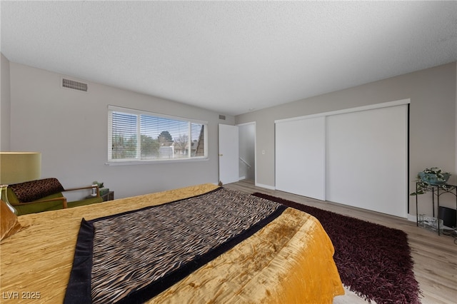bedroom featuring wood finished floors, visible vents, a closet, and a textured ceiling
