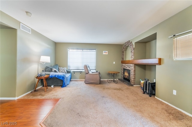 living area featuring baseboards, visible vents, carpet flooring, and a stone fireplace