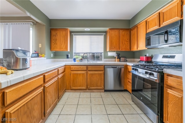 kitchen featuring tile countertops, stainless steel appliances, and brown cabinetry