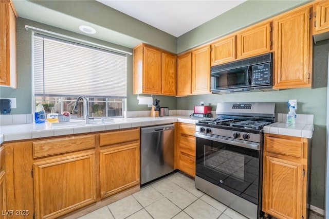 kitchen with light tile patterned floors, tile countertops, appliances with stainless steel finishes, brown cabinets, and a sink