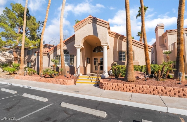 view of front of property with uncovered parking, french doors, a tiled roof, and stucco siding