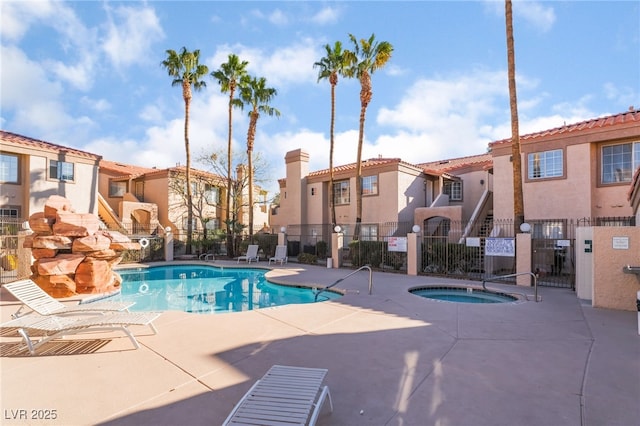 pool with a community hot tub, a patio, fence, and a residential view