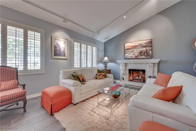 living room with light wood finished floors, a tiled fireplace, vaulted ceiling, and a wealth of natural light