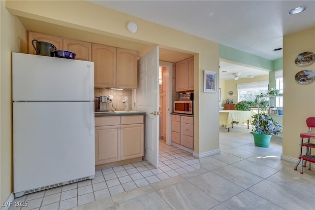 kitchen with light countertops, stainless steel microwave, decorative backsplash, light brown cabinetry, and freestanding refrigerator