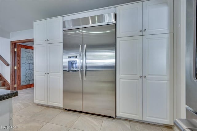 kitchen with light tile patterned floors, dark stone counters, white cabinetry, and stainless steel built in fridge