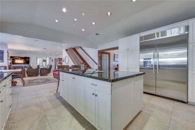 kitchen with white cabinetry, vaulted ceiling, a kitchen island, dark stone counters, and built in refrigerator