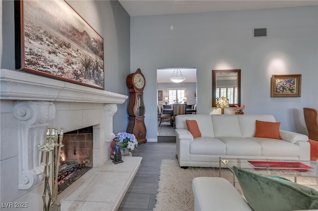 living area with baseboards, visible vents, a fireplace with raised hearth, and wood finished floors