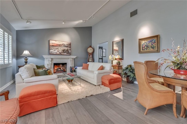 living area with a fireplace, lofted ceiling, visible vents, track lighting, and light wood-type flooring