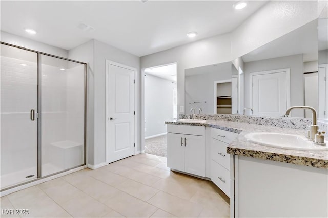 bathroom with double vanity, a shower stall, a walk in closet, and a sink