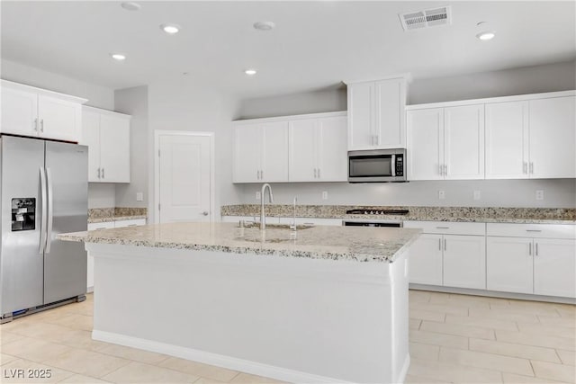 kitchen with a kitchen island with sink, stainless steel appliances, a sink, white cabinets, and light stone countertops