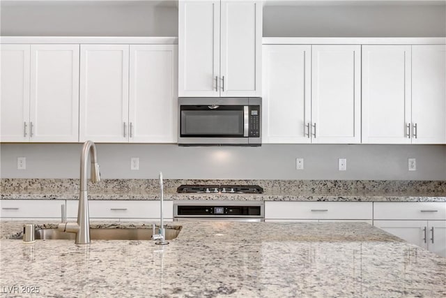 kitchen featuring appliances with stainless steel finishes, white cabinetry, a sink, and light stone countertops