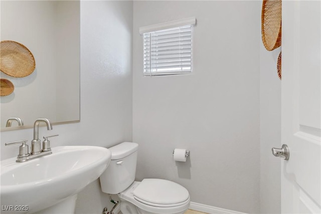 half bathroom featuring a sink, toilet, and baseboards