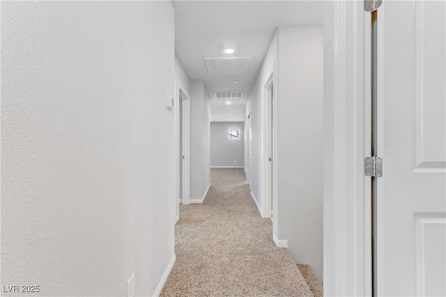 hallway with light colored carpet, visible vents, and baseboards