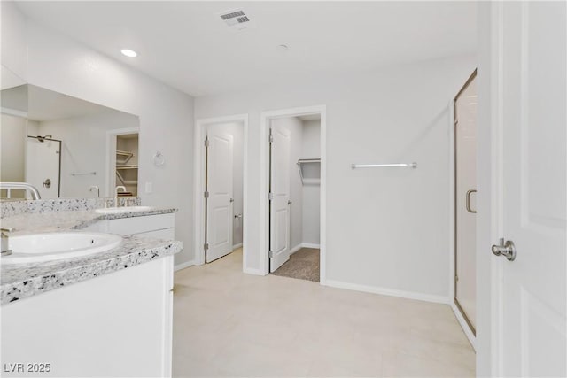 bathroom featuring a spacious closet, a stall shower, a sink, and visible vents