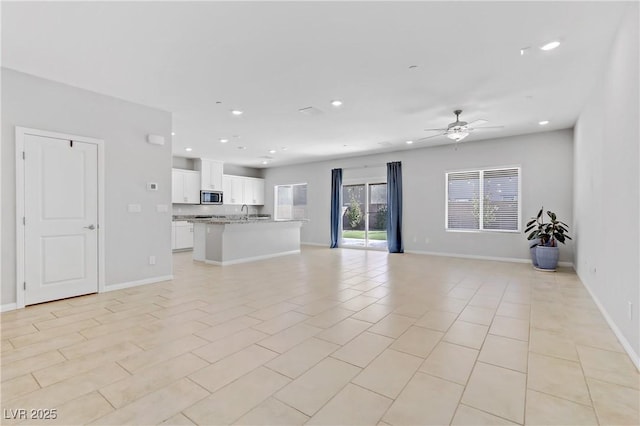 unfurnished living room with ceiling fan, baseboards, a sink, and recessed lighting