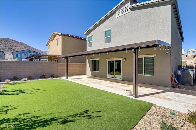 rear view of house with cooling unit, fence, a lawn, stucco siding, and a patio area