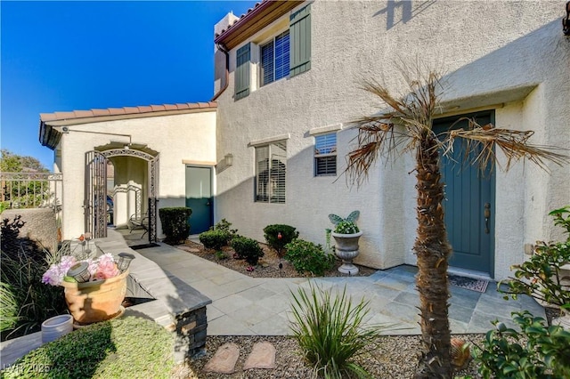 view of exterior entry featuring a patio, fence, a tile roof, and stucco siding