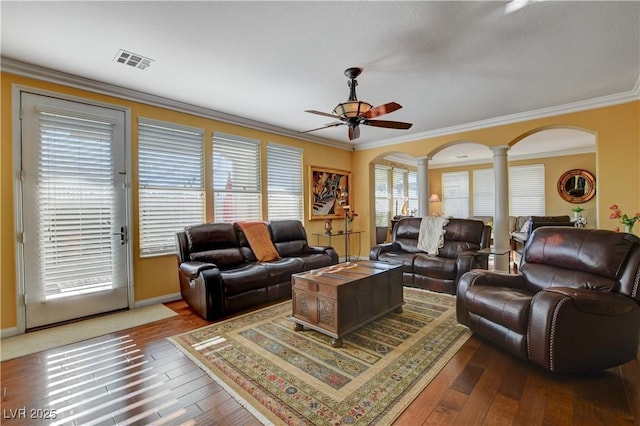 living area with visible vents, arched walkways, dark wood-type flooring, crown molding, and ornate columns