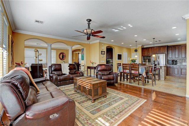 living area with visible vents, arched walkways, light wood-style floors, ceiling fan, and ornate columns