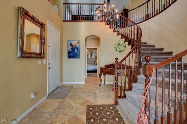 entrance foyer featuring arched walkways, a high ceiling, a notable chandelier, and baseboards