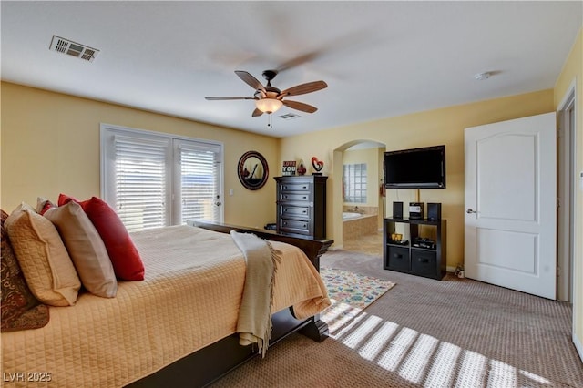 bedroom with arched walkways, carpet flooring, visible vents, and connected bathroom