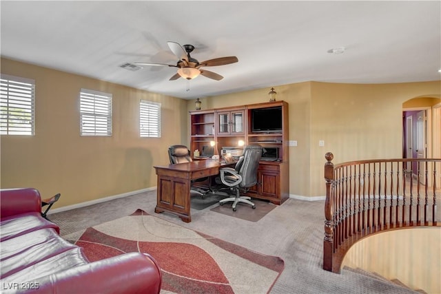 office space featuring light carpet, baseboards, visible vents, arched walkways, and ceiling fan