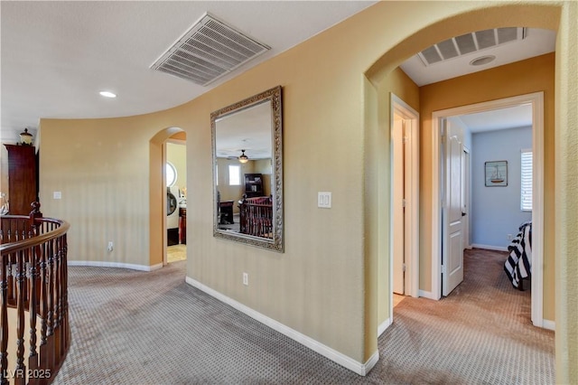 corridor with baseboards, visible vents, arched walkways, and carpet flooring