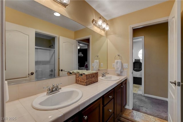 full bathroom with double vanity, an enclosed shower, baseboards, and a sink