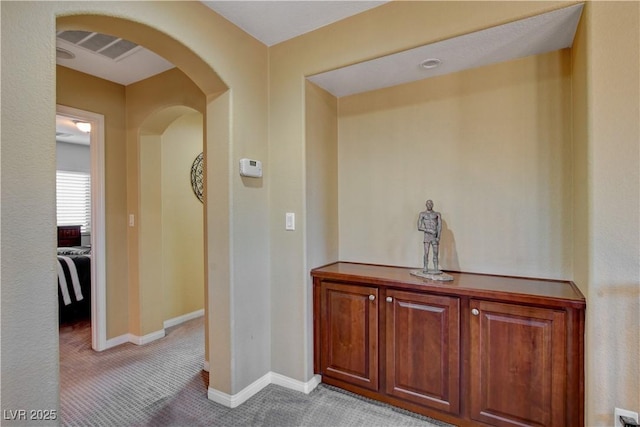 hallway with arched walkways, light carpet, visible vents, and baseboards