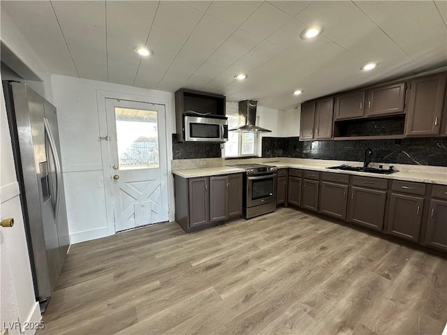 kitchen featuring light countertops, appliances with stainless steel finishes, light wood-style floors, a sink, and wall chimney range hood