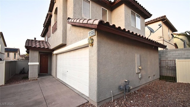 view of home's exterior featuring a tile roof, fence, concrete driveway, and stucco siding