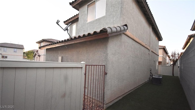 view of side of home with central air condition unit, a tiled roof, fence, and stucco siding