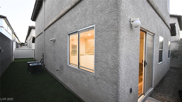 view of side of home with central air condition unit, fence, and stucco siding