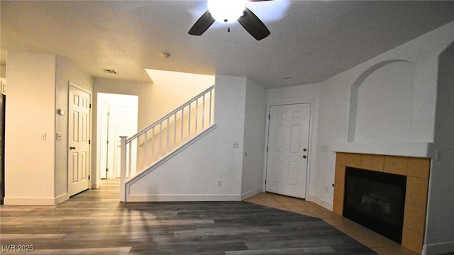 unfurnished living room with a tile fireplace, wood finished floors, visible vents, baseboards, and stairway