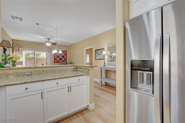 kitchen featuring light stone counters, light wood-style flooring, visible vents, white cabinets, and stainless steel fridge