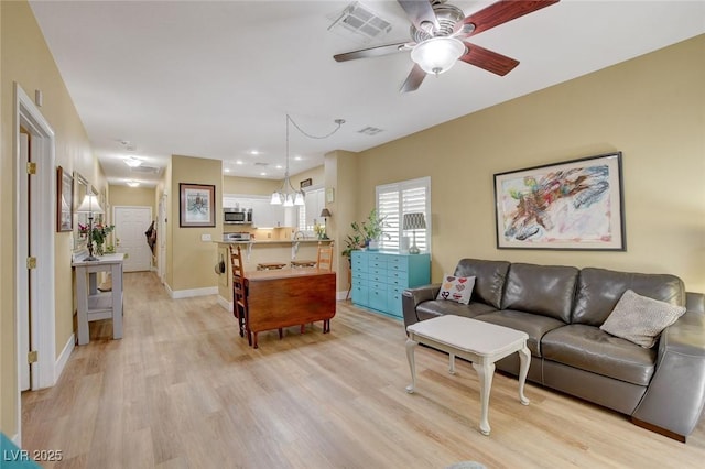 living room featuring baseboards, visible vents, ceiling fan, stairway, and light wood-type flooring