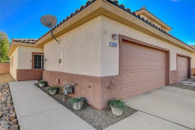 view of home's exterior featuring driveway, a tiled roof, an attached garage, and stucco siding