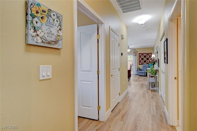 hallway with light wood-style floors, visible vents, and baseboards