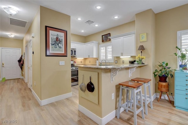 kitchen featuring appliances with stainless steel finishes, visible vents, a breakfast bar area, and light stone countertops