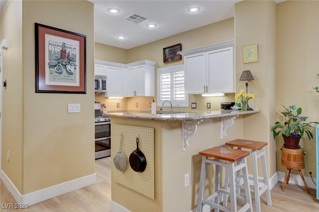 kitchen featuring stainless steel appliances, visible vents, a kitchen bar, and white cabinetry