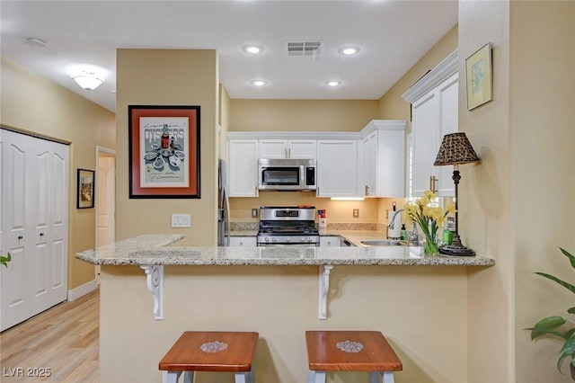 kitchen featuring visible vents, appliances with stainless steel finishes, white cabinetry, a sink, and light stone countertops